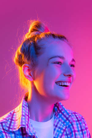 Portrait of adorable young girl, student with wearing plaid shirt isolated on magenta color background in neon light. Concept of beauty, art, fashion, emotionsの写真素材