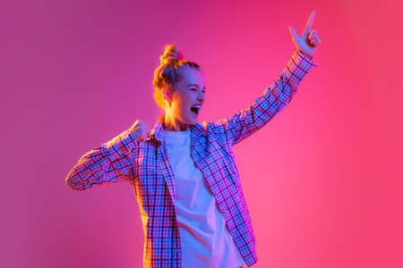 Astonished young girl, student wearing plaid shirt isolated on magenta color background in neon light. Concept of beauty, art, fashion, emotionsの写真素材