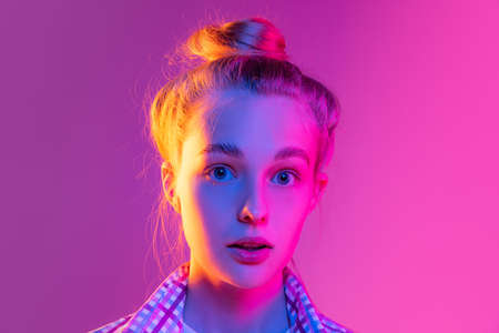 Closeup face of young surpised girl, student looking at camera isolated on magenta color background in neon light. Concept of beauty, art, fashion, emotionsの写真素材