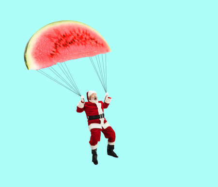 Contemporary art collage. Creative design. Cheerful senior man in image of Santa Claus flying on watermelon like paragliderの写真素材