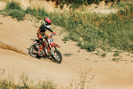 Dnipro, Ukraine JULY 01, 2022. Ukrainian beginner motorcycle rider driving on Enduro motorbike, outdoors at hot summer day. Kids motocross trainingのeditorial素材