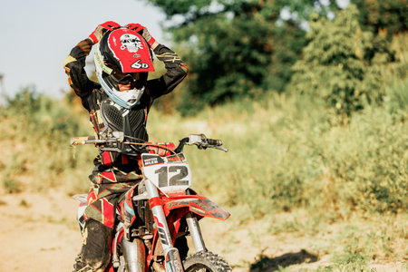 Dnipro, Ukraine JULY 01, 2022. Ukrainian beginner motorcycle rider driving on Enduro motorbike, outdoors at hot summer day. Kids motocross trainingのeditorial素材