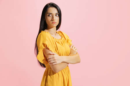 Portrait of young beautiful serious woman in summer yellow dress isolated on pink background. Concept of beauty, art, fashion, human emotionsの写真素材