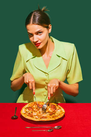 Young woman eating delicious Italian pizza isolated over green background. Traditional mealの写真素材