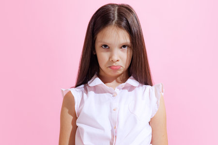 Portrait of little cute offended girl, kid in blouse isolated on pink background. Concept of children emotions, fashion, beauty, school and adの写真素材