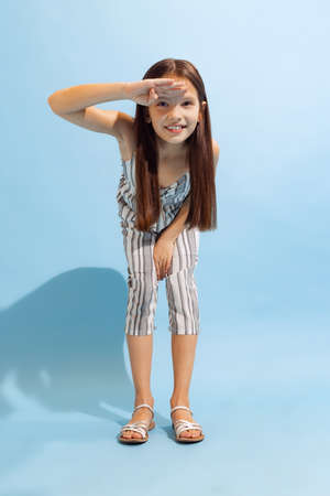 Pretty school-age girl, kid in summer clothes posing isolated on light blue background. Concept of...