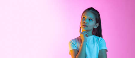 Flyer with portrait of cute school age girl, kid wearing white t-shirt isolated on pink background in neon. Concept of emotions, fashion, beauty, school and adの写真素材