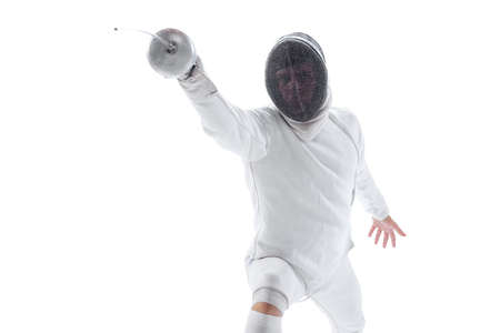 Dynamic portrait of young man, fencer in in fencing costume with sword in hand training isolated on...
