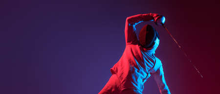 Male fencer with smallsword practicing fencing isolated on purple background in neon light. Sport, energy, skills, achievementsの写真素材