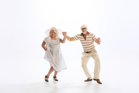 Portrait of retro style dancers, senior man and woman in vintage attire dancing swing isolated on...