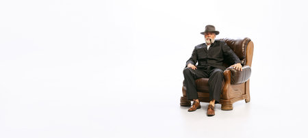 Portrait of stylish senior man in retro style clothes, vintage outfit sitting at armchair isolated on white background. Concept of culture, art, fashion style, adの写真素材