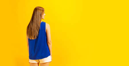 Back view of young girl with long glossy light hair isolated on bright yellow background. Concept of...