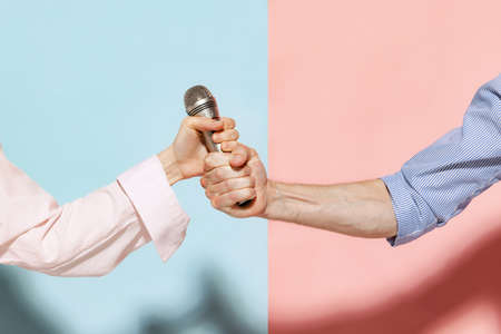 Closeup male and female hands holding microphone isolated over blue and pink background. Emotions, youth, love and diversity conceptの写真素材