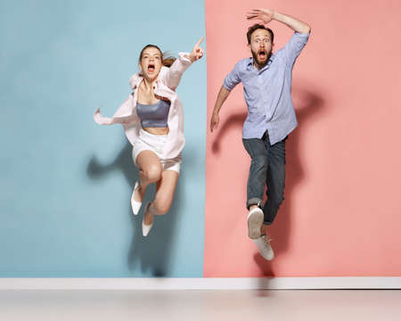 Astonished man and woman running, jumping isolated over blue and pink background. Human emotions, youth, love and active lifestyle conceptの写真素材