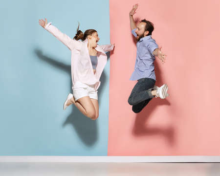 Astonished man and woman running, jumping isolated over blue and pink background. Human emotions, youth, love and active lifestyle conceptの写真素材