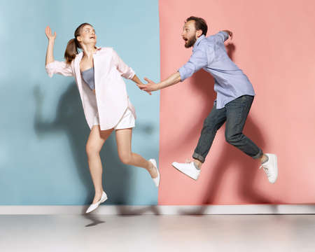 Astonished man and woman running, jumping isolated over blue and pink background. Human emotions, youth, love and active lifestyle conceptの写真素材