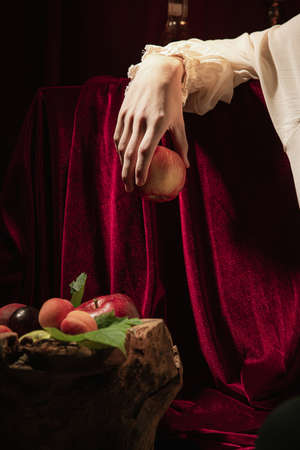 Closeup male hand with red apple over dark vintage background. Italian baroque style, art, creativity, vintageの写真素材