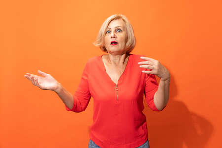 Half-length portrait of beautiful middle age woman with blond hair posing isolated on orange color background. Concept of emotions, facial expressionsの写真素材