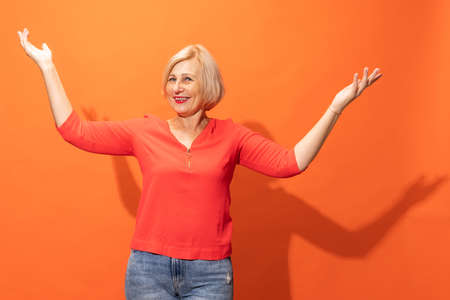 One excited beautiful middle age woman with blond hair posing isolated on orange color background....