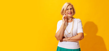 Studio shot of fashionable senior woman in summer style outfit isolated on bright yellow background....