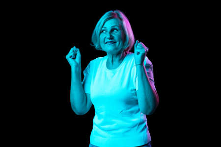 Half-length portrait of caucasian senior woman with blond hair posing isolated over dark background in neon light. Concept of emotions, facial expressionsの写真素材