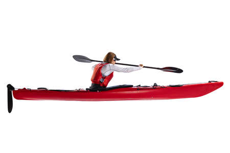 Profile view. Female sportsman in red canoe, kayak with a life vest and a paddle isolated on white background. Concept of sport, nature, travel, active lifestyleの写真素材