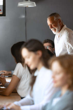 Impressive senior man, professor helds master class, workshop for his students, young employees in loft style office. Concept of business, studying, careerの写真素材