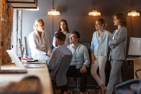 Senior man, manager sharing ideas, plans and thoughts about project to his partners, co-workers in loft style office.の写真素材
