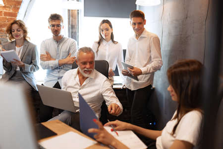 Senior man, manager sharing ideas, plans and thoughts about project to his partners, co-workers in loft style office.の写真素材