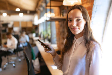 Beautiful young confident woman at loft style office with group of colleagues in background. Concept of success, business, career, achievementsの写真素材