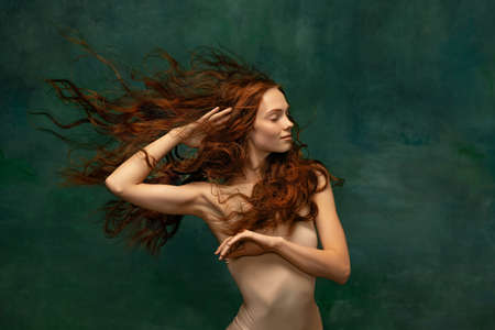 Adorable tender redhead girl with long curly hair isolated over dark green background. Fabolous curly hair and harming gaze. Concept of beauty, artの写真素材