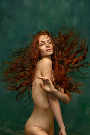 Adorable tender redhead girl with long curly hair isolated over dark green background. Fabolous curly hair and harming gaze. Concept of beauty, artの写真素材
