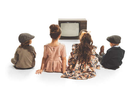 Group of fashionable kids, children sitting in front of retro tv set isolated on white background. Vintage style concept. Friendship, hobbies, artの写真素材