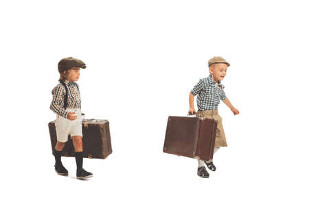 Portrait of cute little boys, happy kids going with retro suitcase isolated on white studio background. Retro vintage style concept. Holidays, vacation, tripの写真素材