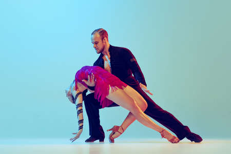 Dynamic portrait of professional dancers in stage attires dancing ballroom dance isolated on blue background. Concept of art, beauty, music, style.の写真素材