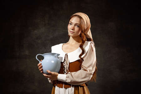 Vintage style. Young charming redhair girl with long curly hair like girl of renaissance eras isolated on dark background. Eras comparison, beauty, art, paintingの写真素材