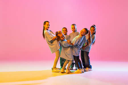 Dance group of happy, active little girls in t-shirts and jeans in action isolated on orange background in neon. Concept of music, fashion, art, childhoodの写真素材