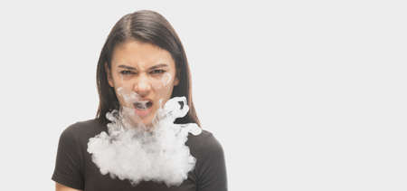 Angry young girl with dark hair releases smoke from the mouth isolated over white background....