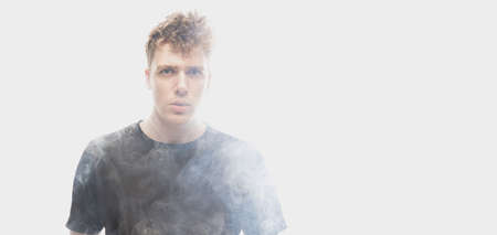 Smoke enveloped young man. Model looking at camera isolated over white background with clouds of...