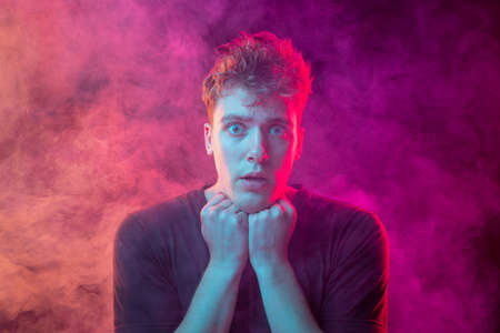 Smoke enveloped young man. Model looking at camera isolated over magenta background with clouds of smoke. Concept of mental health, art, emotionsの写真素材