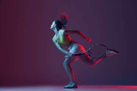 Full length portrait of young woman playing tennis isolated on dark background in neon. Healthy lifestyle, fitness, sport, exercise concept.の写真素材