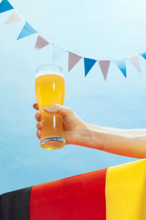 Human hand holding glass of cold light beer over summer blue sky background. Oktoberfest, vacation,...
