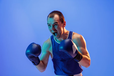 Winner emotions. Male boxer in blue uniform and boxing gloves shouting isolated on blue background in neon. Strength, attack and motion concept.の写真素材
