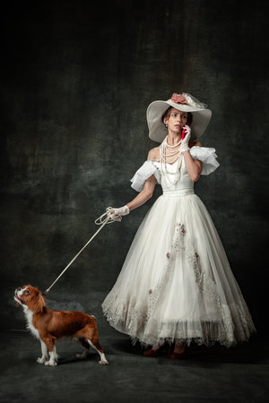 Lady with dog. Vintage portrait of young elegant woman in image of medieval person in renaissance style dress isolated on dark background.の写真素材