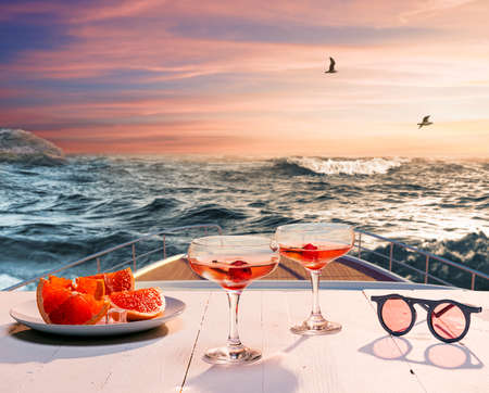 Romantic evening sea trip. Cocktail glasses, fruit on deck of private yacht during honeymoon holidays, outdoors. Love, travel, vivid impressionsの写真素材