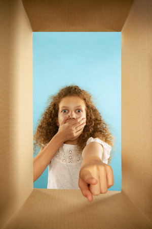 Shocked kid, little girl looking inside box during opening, unpacking it and pointing at gift. Emotions, black friday, holidays, online shopping conceptの写真素材