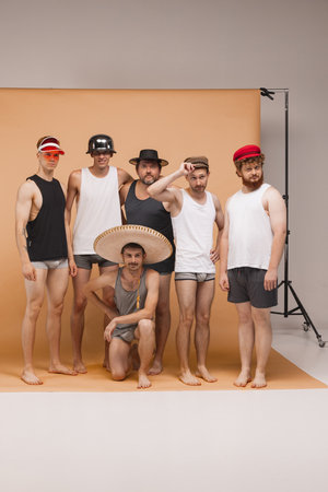 Diversity. Young cheerful people, men of different body types standing together in homewear and hats at studio photo shoot. Concept of art, fashion, friendshipの写真素材