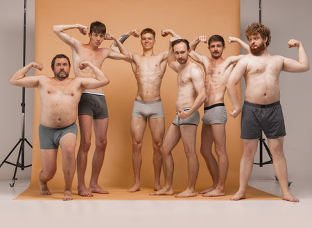 Six young men of different ages having photo shoot at studio. Feeling happy, cheerful and comfortable. Concept of body positive, fashion, friendshipの写真素材