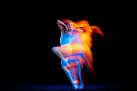 Dynamic portrait of tender slim girl, female ballet dancer in art performance isolated over black background in mixed bright neon light.の写真素材