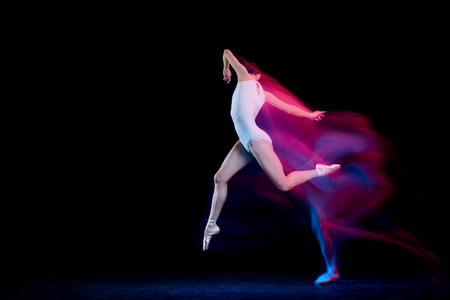 Graceful ballerina dancing on dark background in mixed neon light. Grace, movement, action and motion concept. Looks weightless, flexible.の写真素材